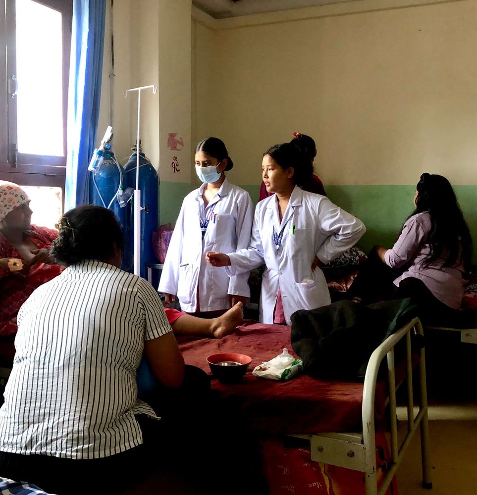 Midwifery students in white coats with patients on a hospital ward